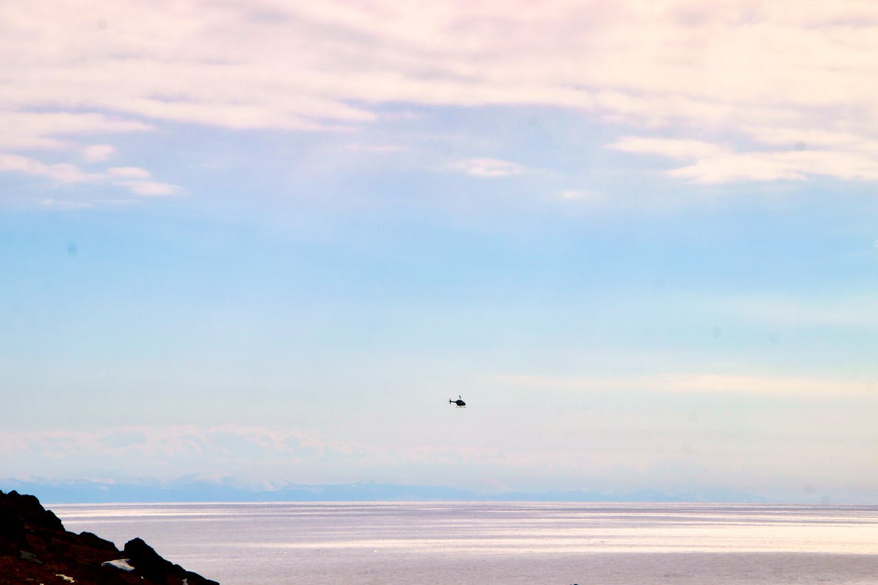 A helicopter flies above a calm ocean during a beautiful sunset, showcasing nature's tranquility.