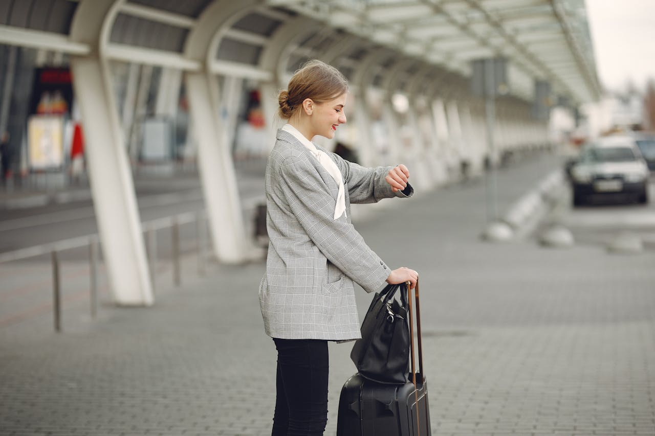 Woman in gray jacket checking wristwatch at station with luggage, representing punctual travel.