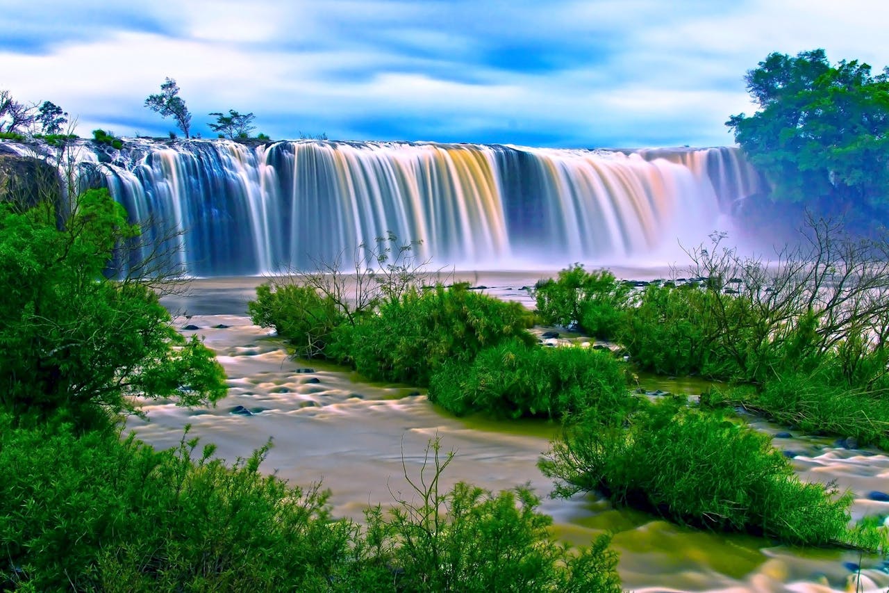 Vibrant waterfall amidst lush greenery under a clear sky, perfect for nature and travel themes.